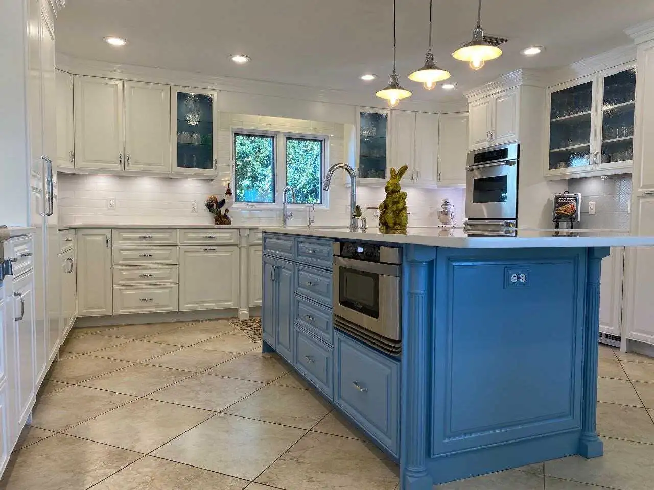 Kitchen cabinet painting in Tampa Bay featuring white custom cabinets, blue island cabinetry, quartz countertops, and tile flooring.