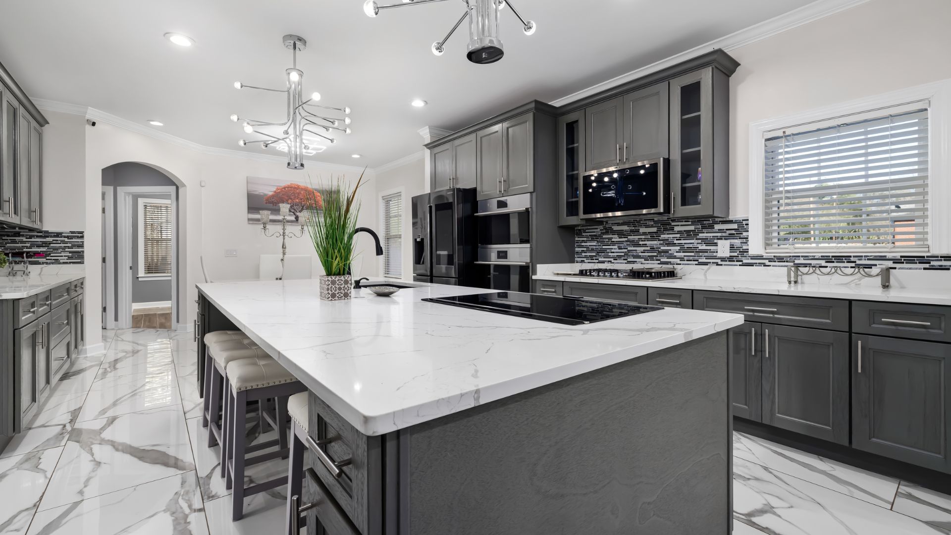 Luxury kitchen and home remodeling featuring gray custom cabinets, large quartz island, and modern tile backsplash.